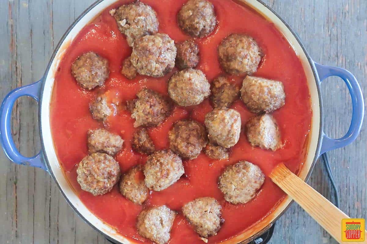 Adding cooked meatballs to pan for meatball sauce recipe
