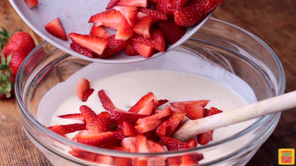 Adding fresh sliced strawberries to Fresas con Crema recipe in a mixing bowl