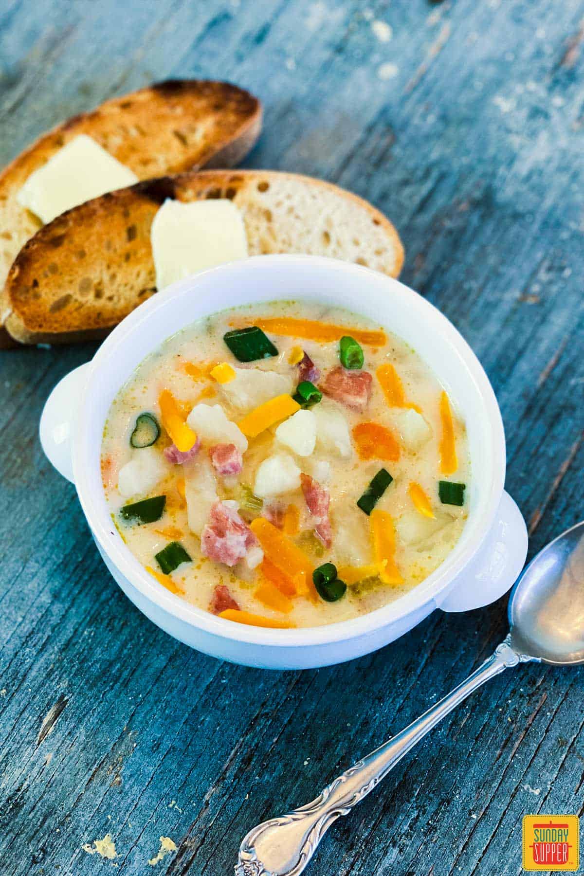 A white bowl of leftover ham soup with two slices of toast and a spoon