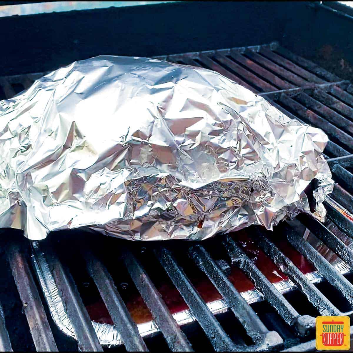 Pork butt wrapped in foil on grill