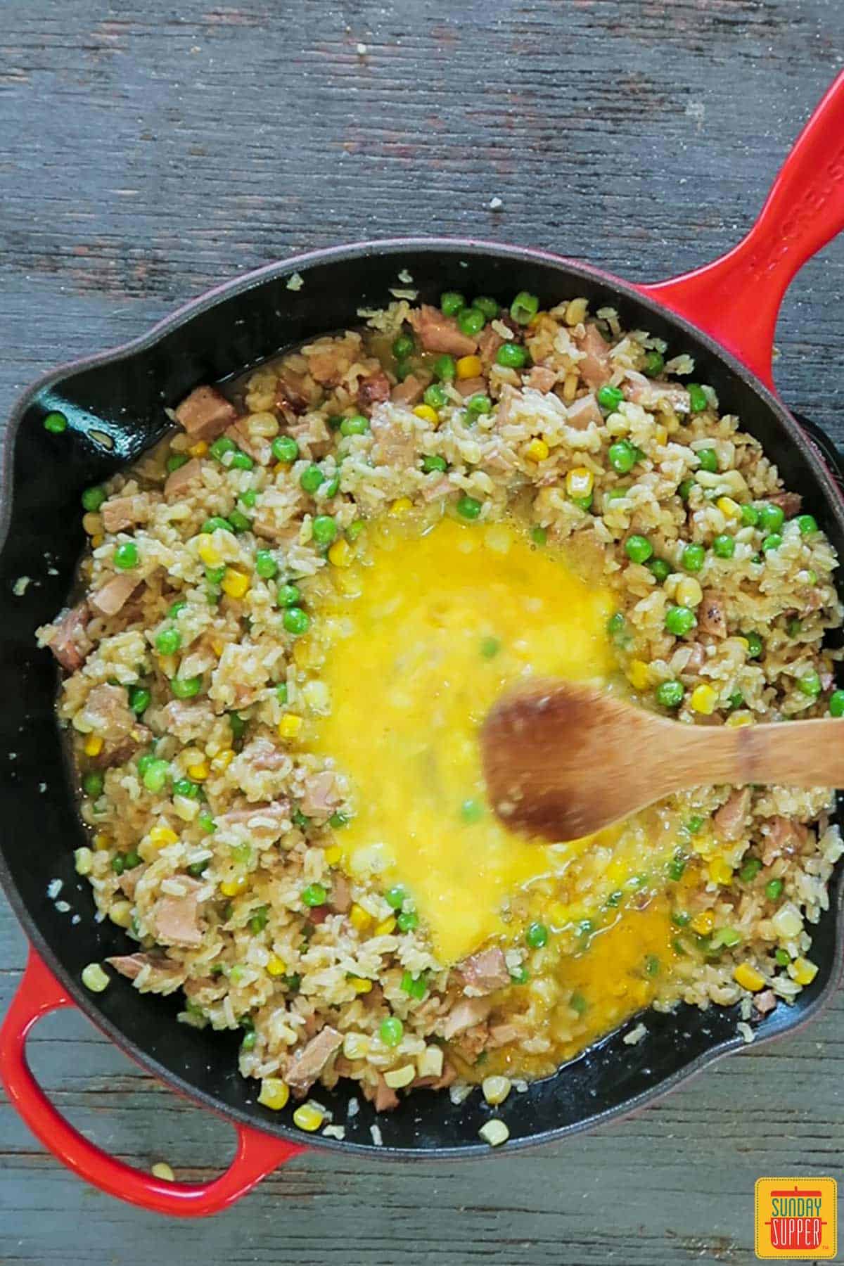 Adding eggs to the well in the fried rice