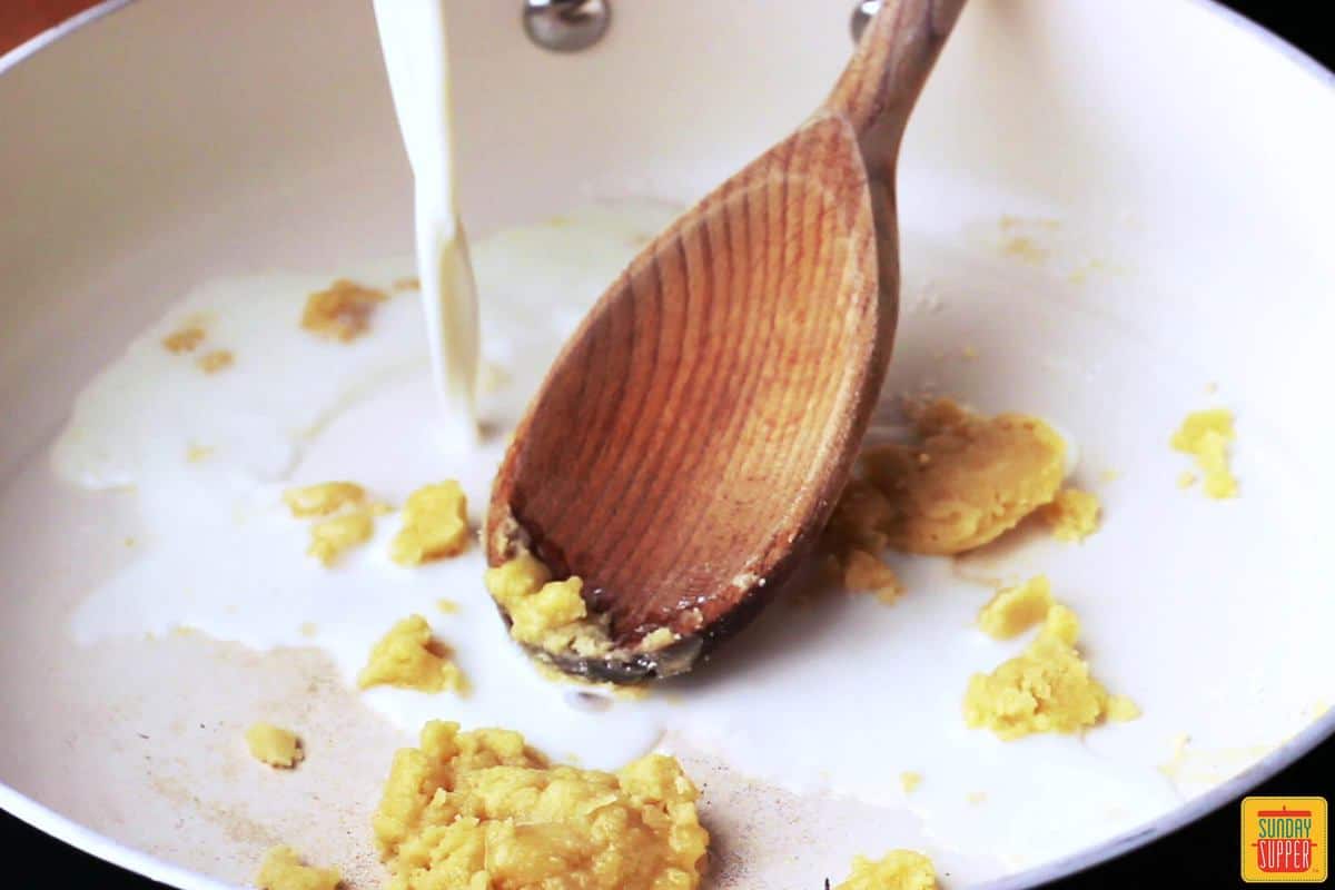 Mixing a roux of flour and butter with milk in a skillet for Rissóis de Camarão