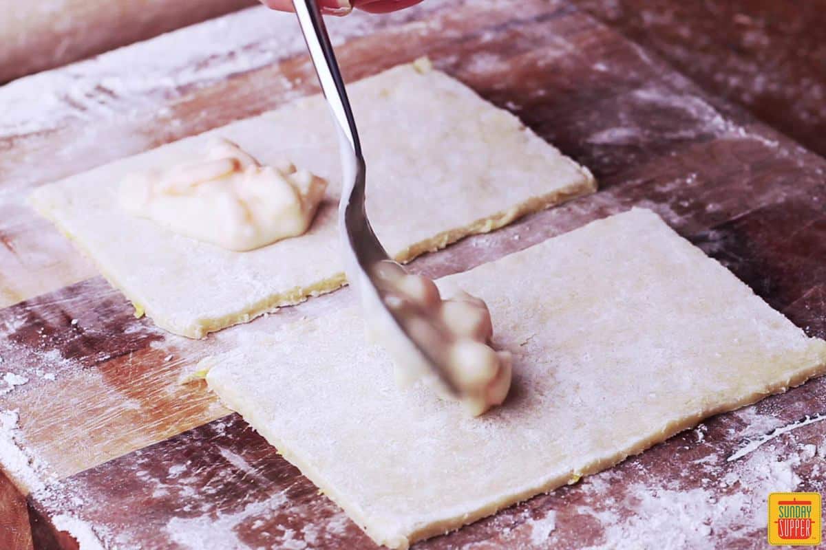 Spooning creamy shrimp filling into the dough to make Rissóis de Camarão