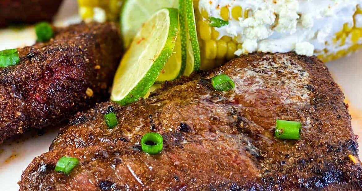 Close up of grilled beef short ribs with lime wedges and elotes Mexicanos