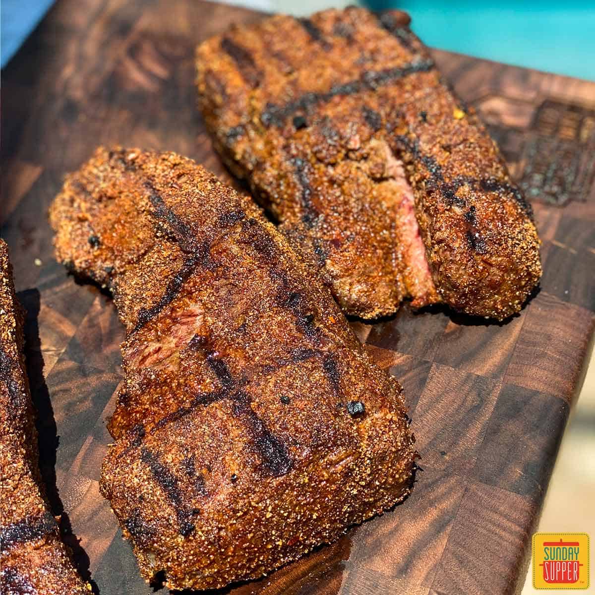 Grilled beef short ribs coated with dry rub for steak on a dark brown cutting board