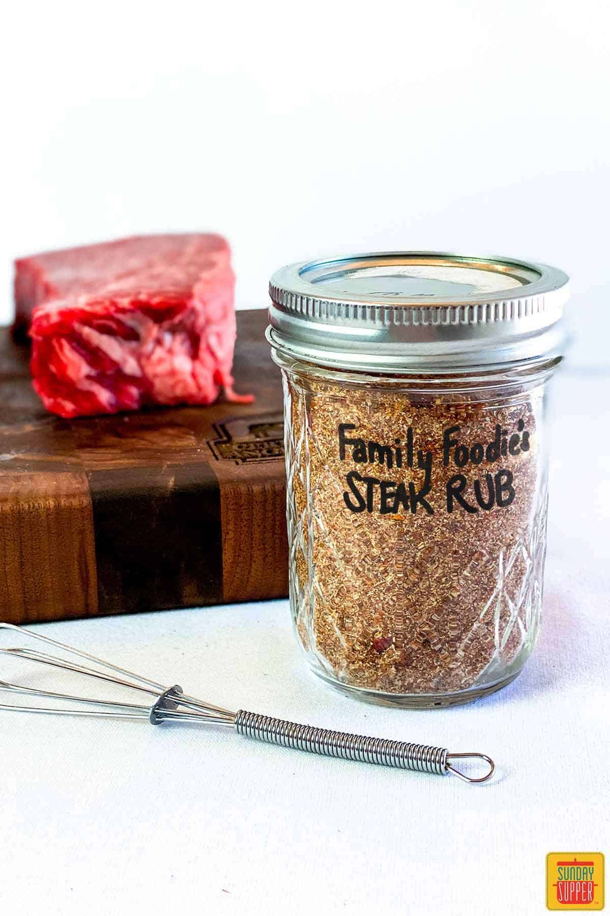 Dry rub for steak seasoning in a mason jar in front of a cutting board with a beef short rib