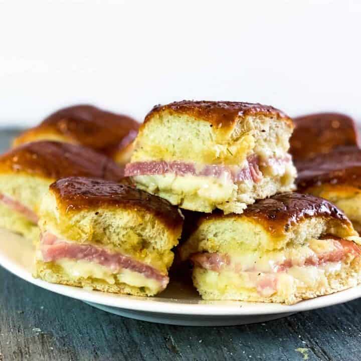 Three leftover ham and cheese sliders on a white plate, stacked on top of each other