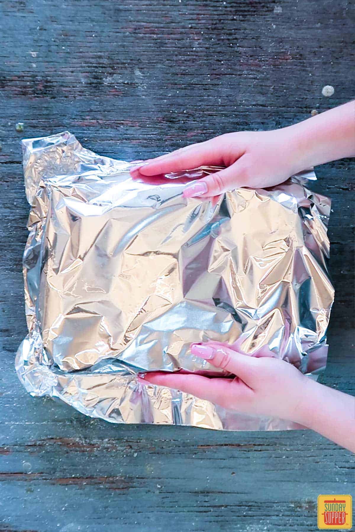 Covering the tray of ham and cheese sliders with aluminum foil