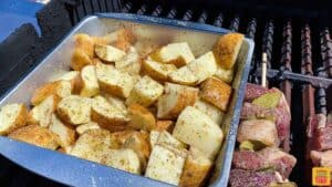 Adding the potatoes to the grill in the baking tin