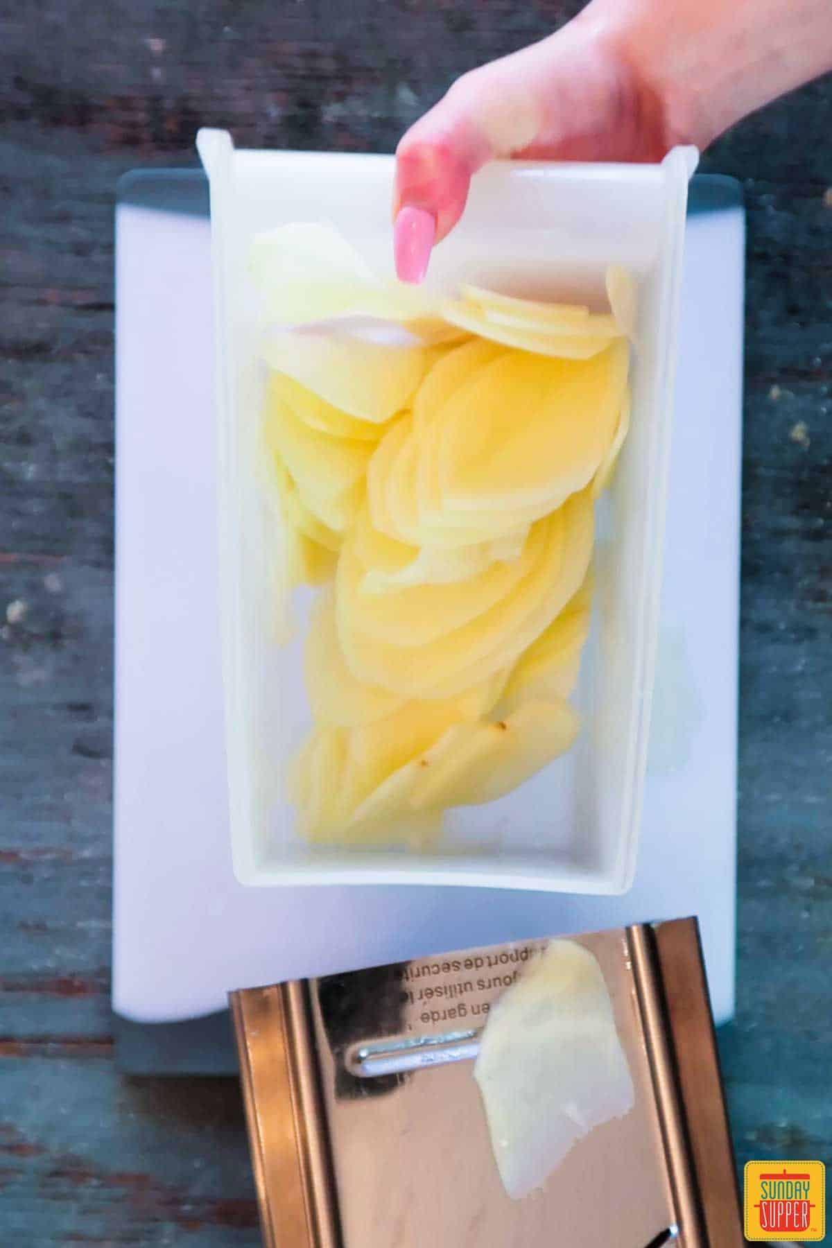 Sliced potatoes in a white dish on a cutting board