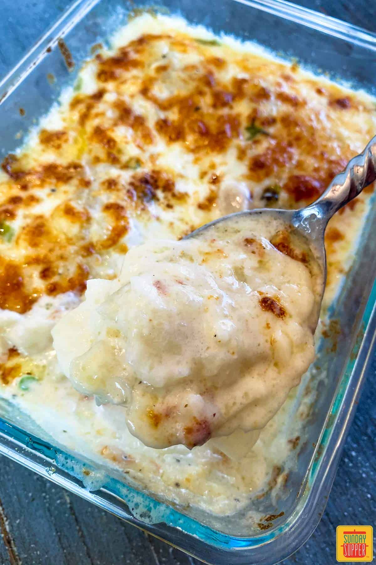 A serving spoon of scalloped potatoes in the glass baking dish