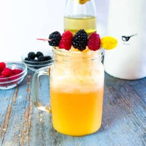 A glass jar of momosa mimosa recipe with fresh berries and a champagne bottle