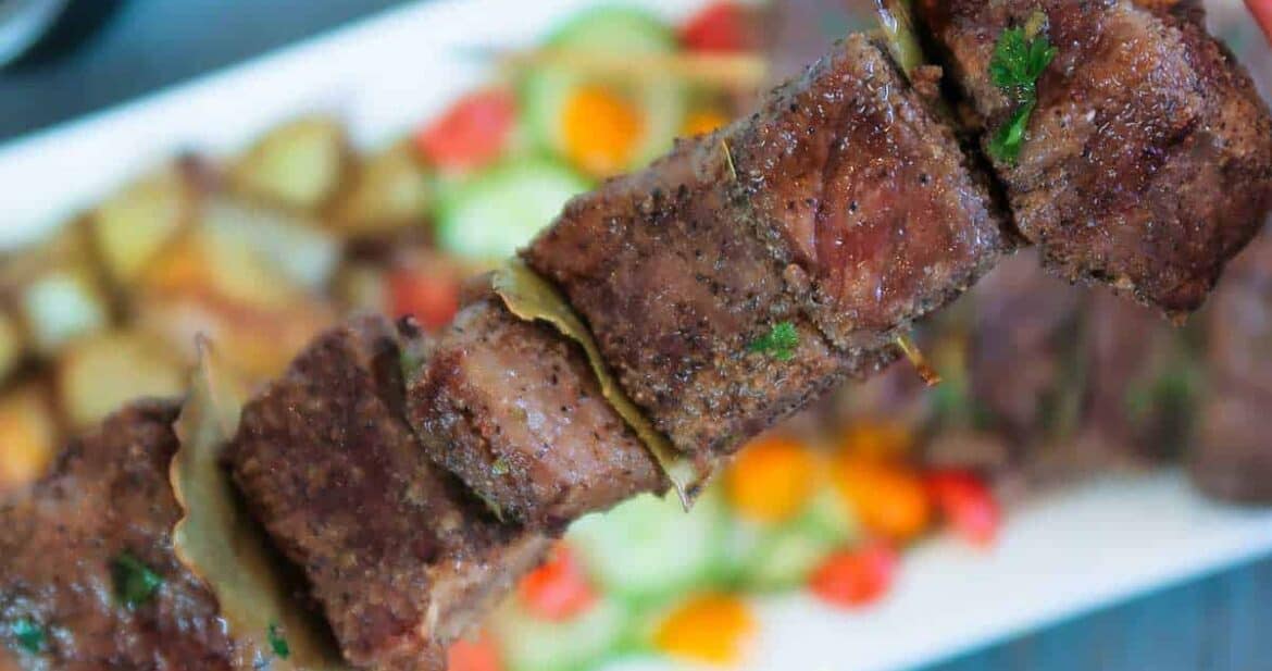 Close up of a cooked beef skewer over a platter of Portuguese beef skewers