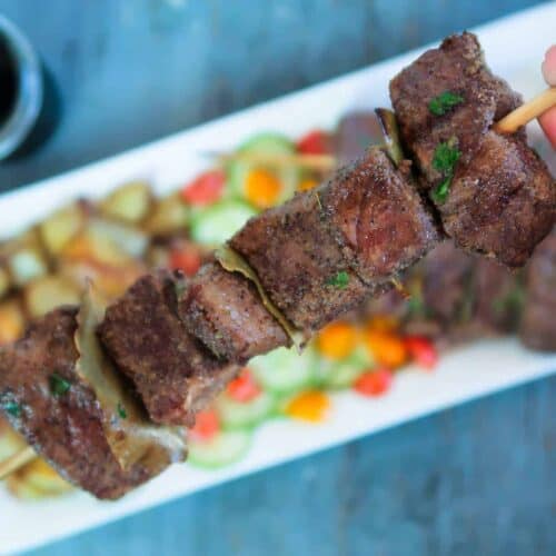 Close up of a cooked beef skewer over a platter of Portuguese beef skewers