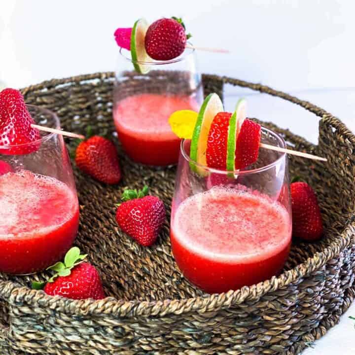 Three glasses of strawberry daiquiri with skewers of fruit on top