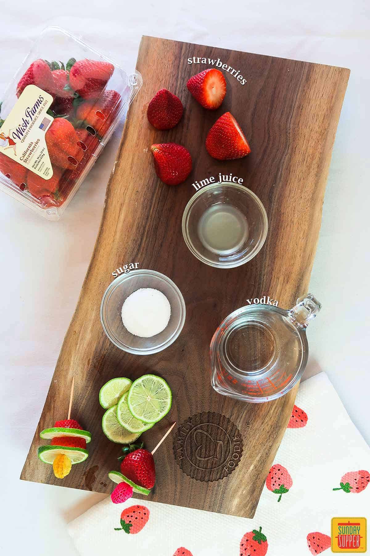 A cutting board with all of the ingredients to make strawberry daiquiri recipe