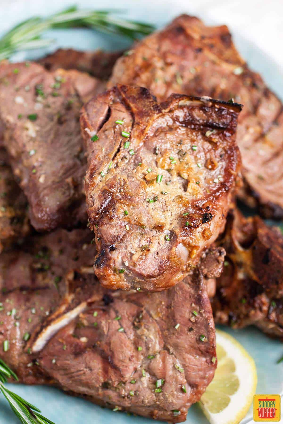 grilled lamb chops stacked on top of each other on a light blue plate with a lemon slice and herbs