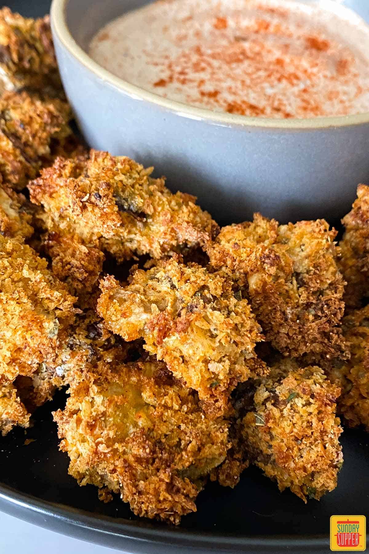 Air fryer mushrooms on a black plate next to dipping sauce in a bowl