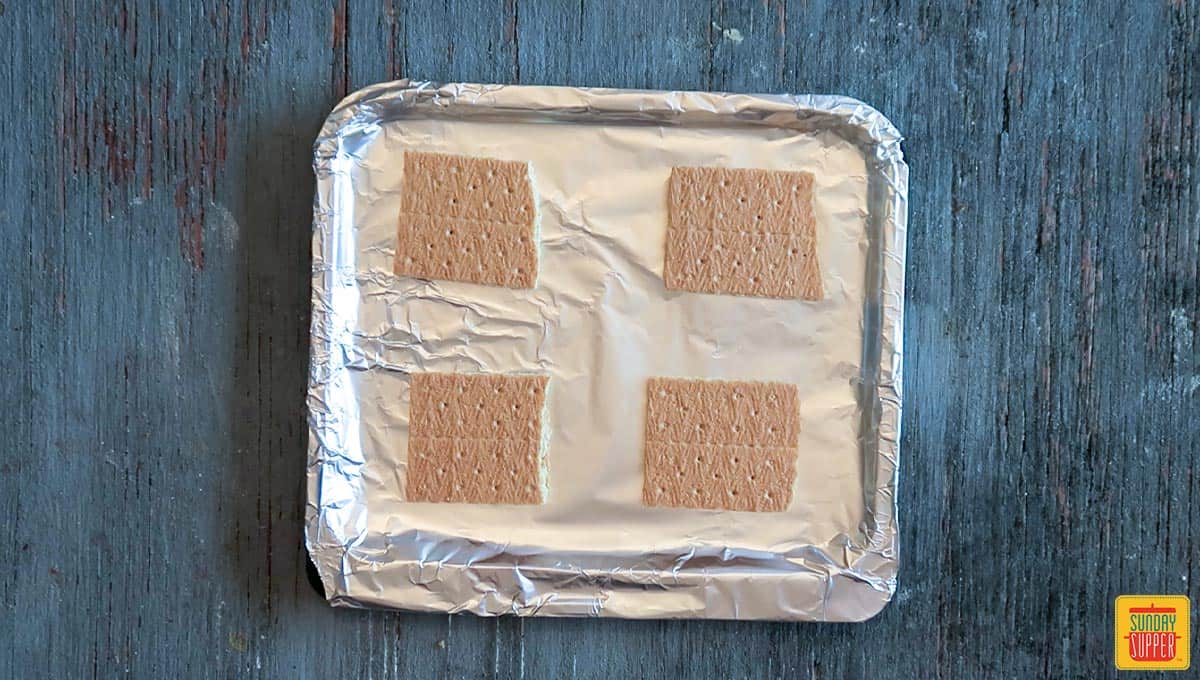 Graham crackers snapped in four halves on an aluminum-foil wrapped air fryer tray in order to make air fryer s'mores recipe