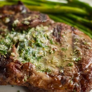 Ribeye steak on a white plate with asparagus and garlic butter melted on top