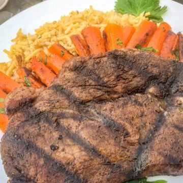 Close up of a Morrocan spiced grilled steak on a plate with carrots, rice, and herbs