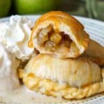 Three caramel apple empanadas up close next to ice cream and whipped cream: the empanada at the top of the stack is cut in half so you can see the apple filling