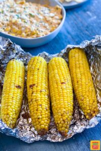 Close up of four grilled corn cobs on a piece of foil