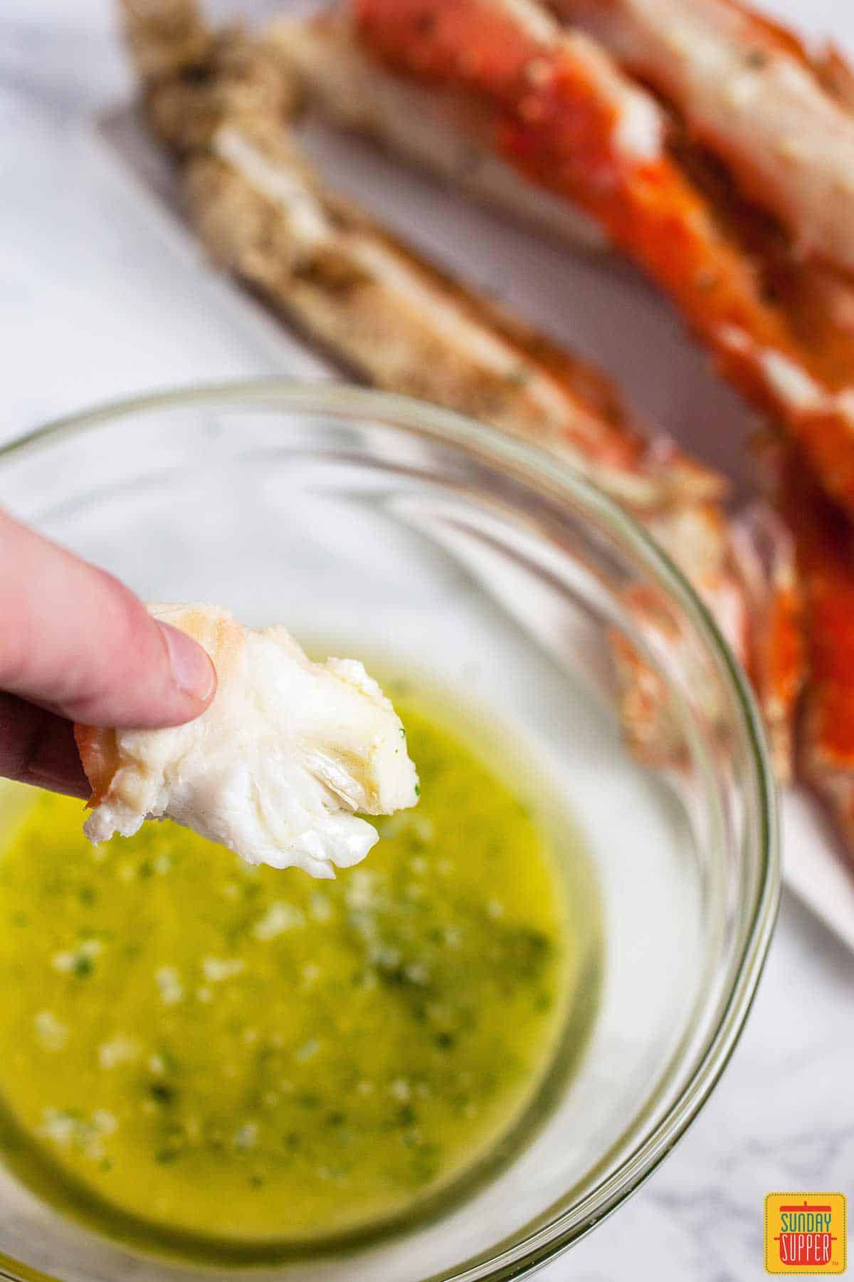 Dipping a piece of crab into garlic butter sauce with grilled crab legs visible in the background