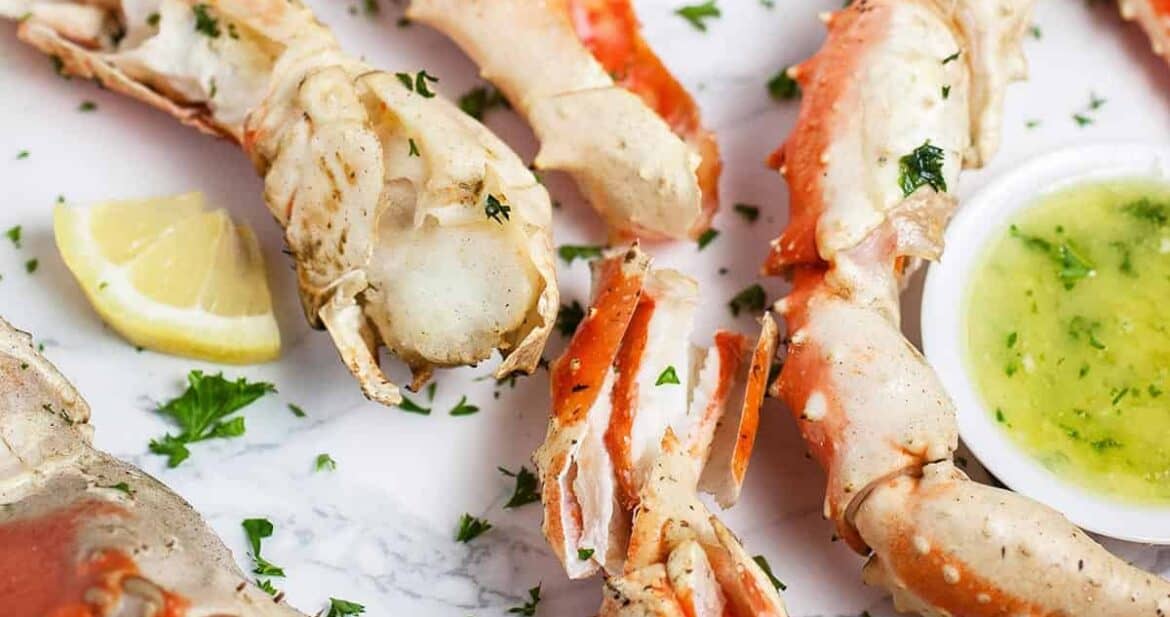 Grilled crab legs on a white surface with fresh herbs and a side of garlic butter in a little bowl