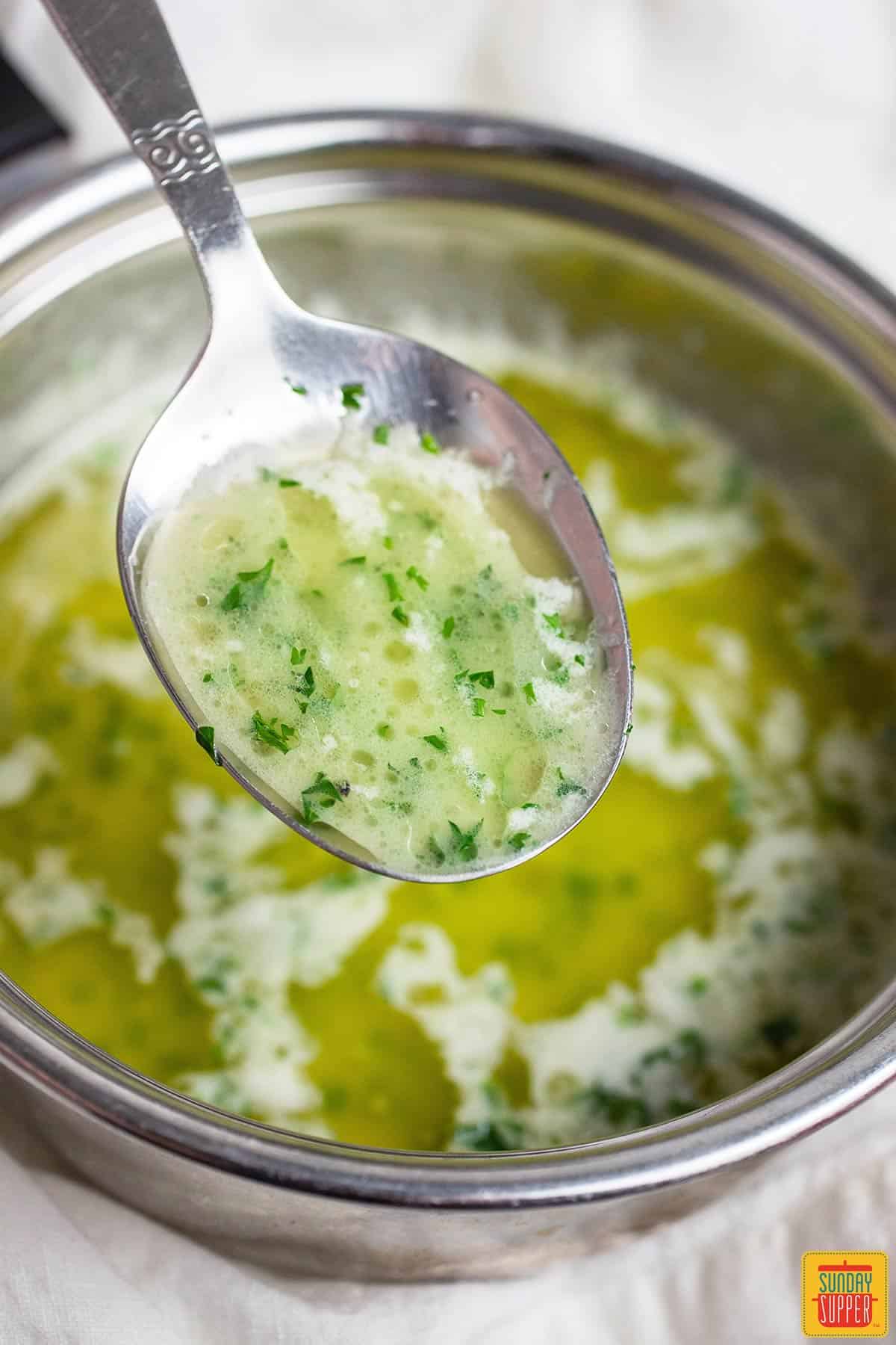 Garlic butter sauce in a metal tin with a spoonful of sauce up close