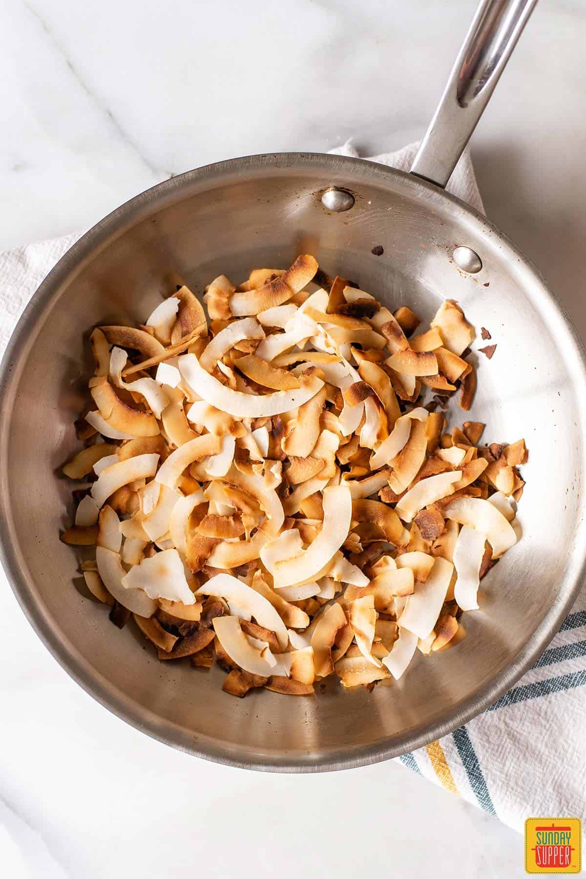 Toasted coconut flakes in a metal skillet