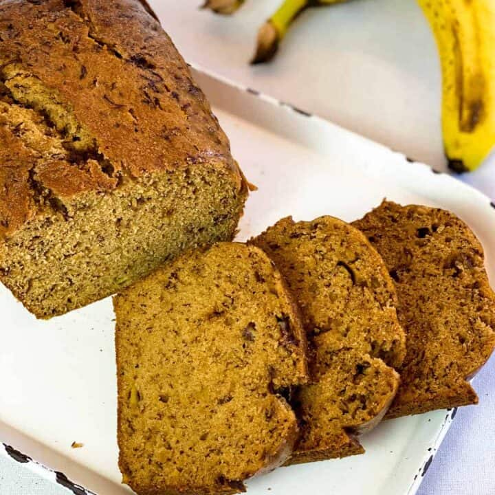 Three slices of Instant Pot Banana Bread next to a loaf of banana bread on a white platter