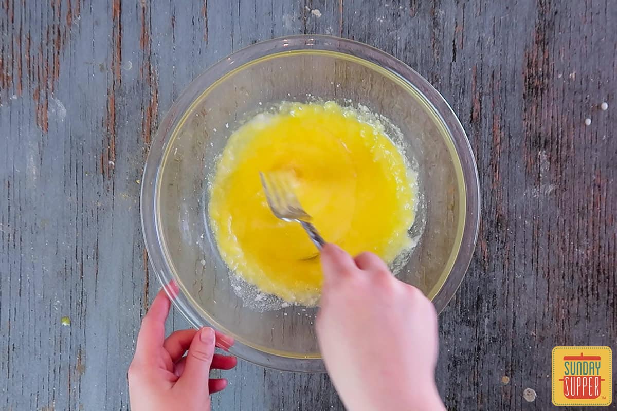 Eggs mixed with creamed butter mixture in a glass bowl, mixing with a fork