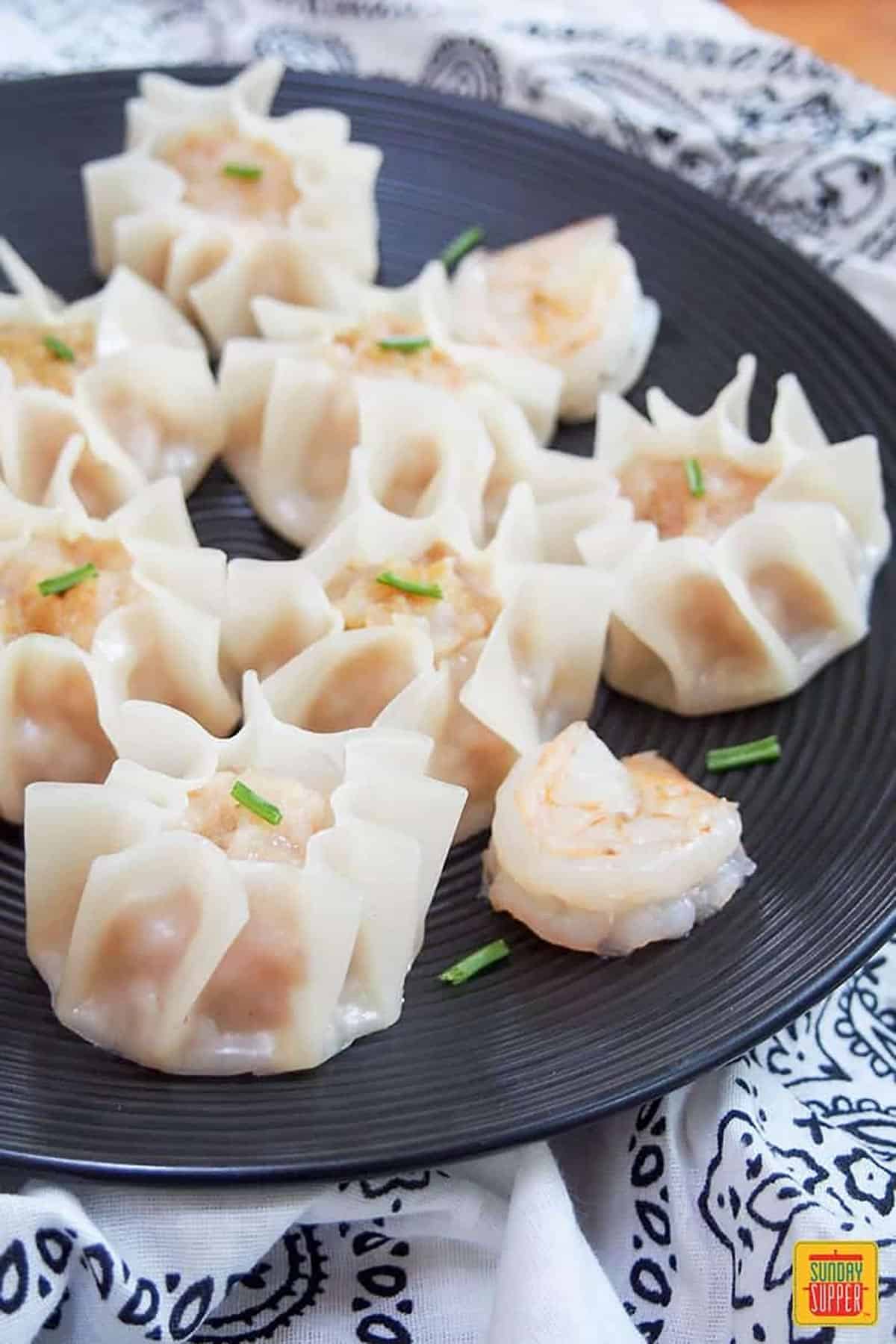 prawn dumplings served on a black plate topped with chives