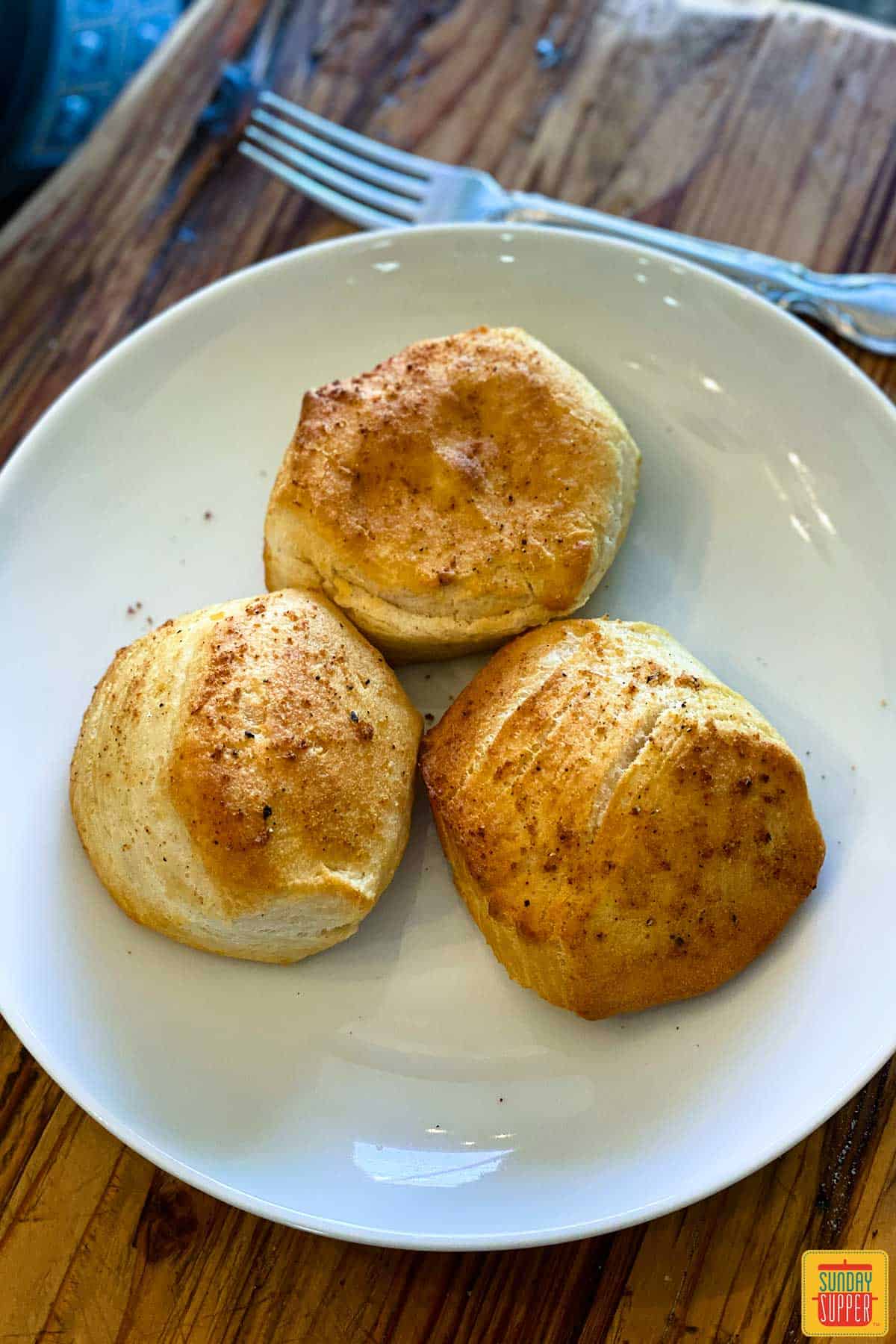 Three air fryer biscuits on a white plate next to a fork