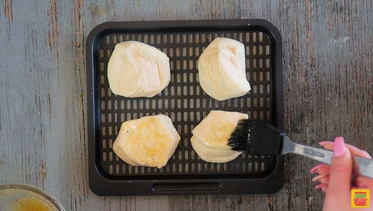 Brushing garlic butter onto four biscuits