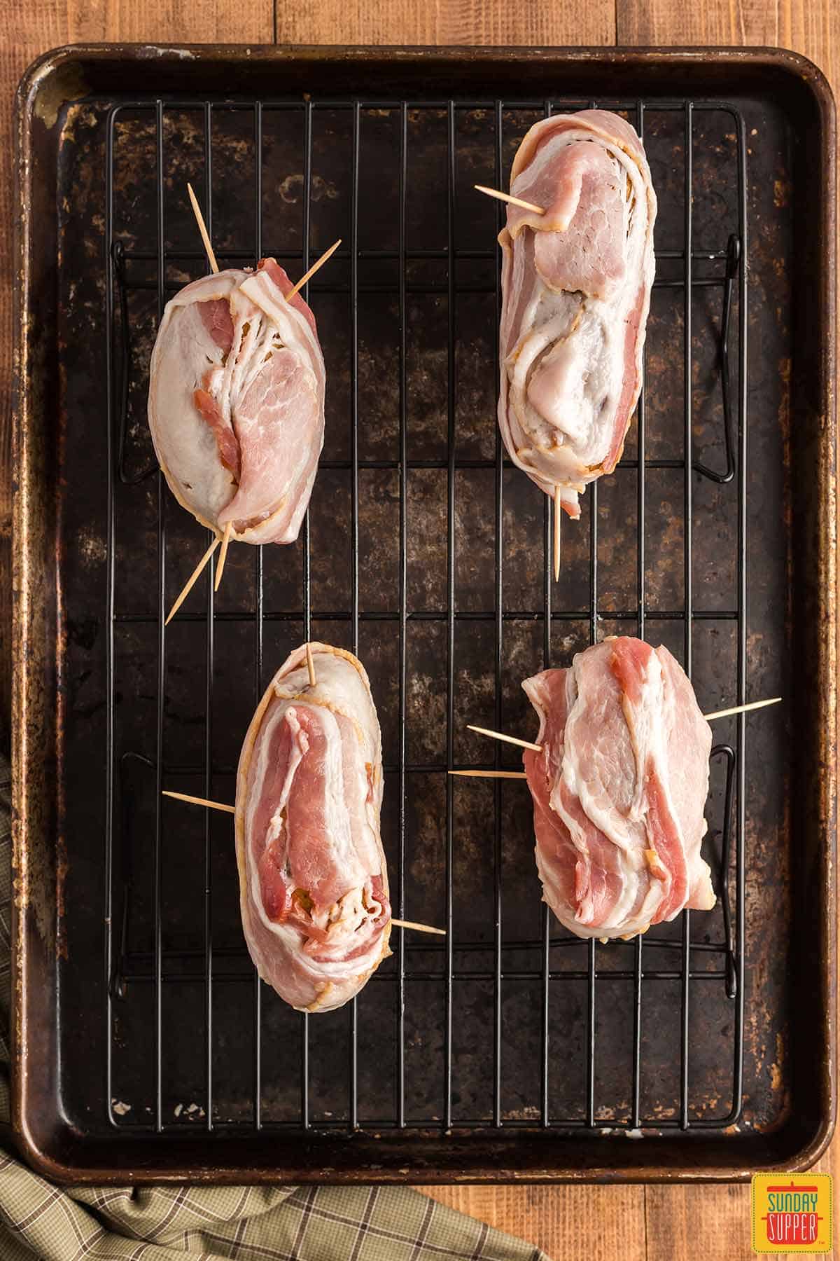 Four potatoes wrapped in bacon set on a rack over a baking sheet