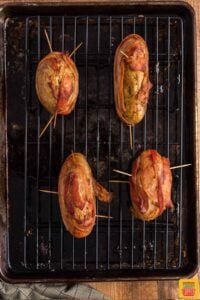 Four crispy potatoes wrapped in bacon on a wire rack over a baking sheet
