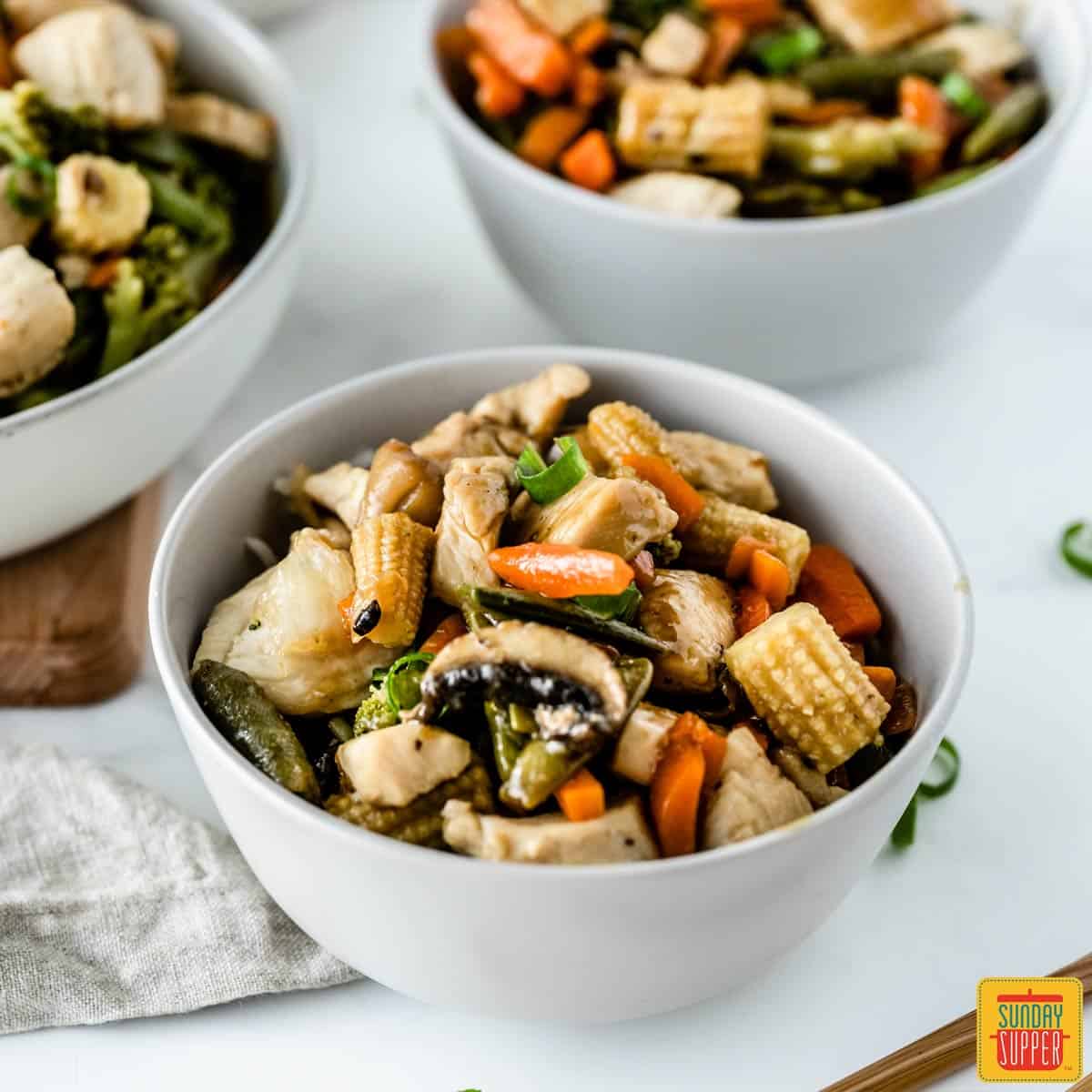 Close up of chicken stir-fry in three white bowls