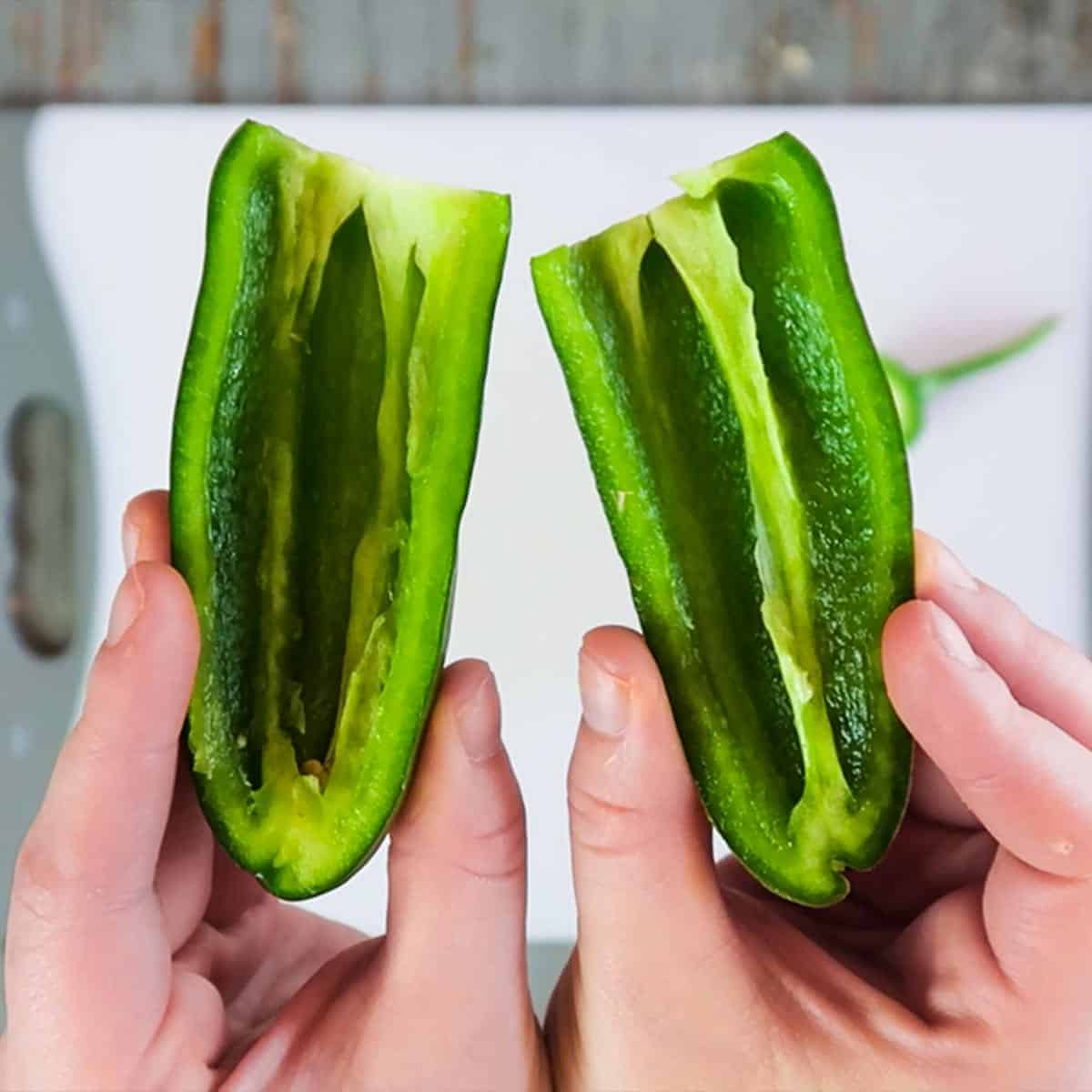 Holding two halves of a jalapeno pepper with the seeds removed for how to cut a jalapeno