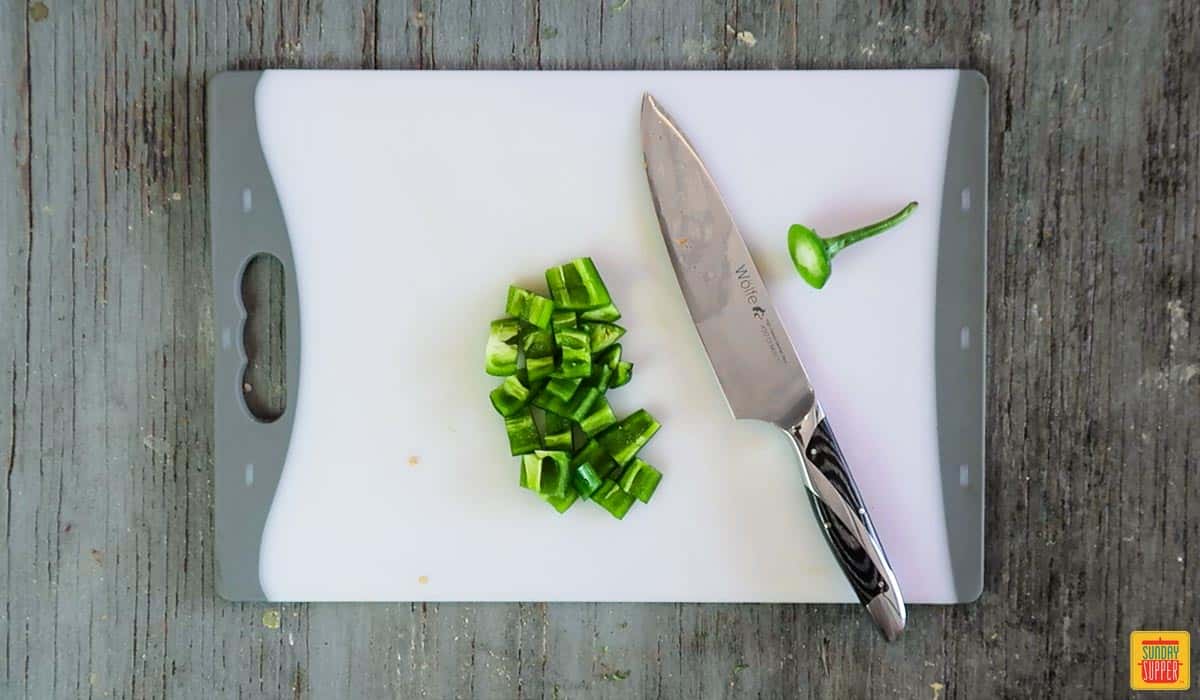 Diced jalapeno in a neat pile on a white cutting board next to a knife
