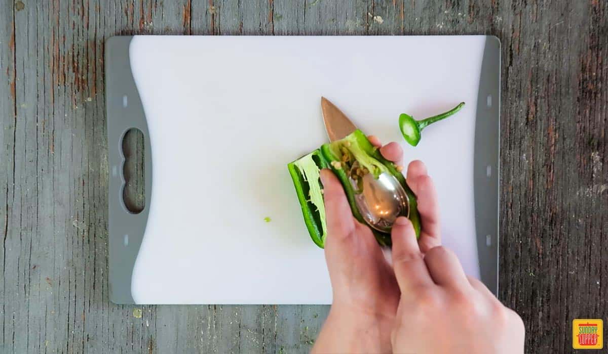 Scooping out any remaining seeds from a jalapeno pepper with a spoon