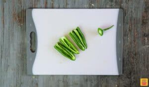 Four jalapeno strips from one whole pepper next to the stem on a cutting board
