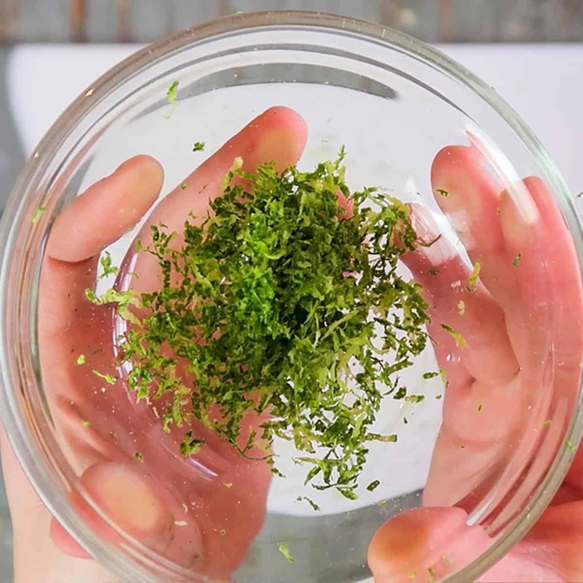 Holding a clear glass bowl with lime zest in both hands