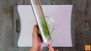 How to zest a lime: running a grater along a lime to release the zest into a glass bowl over a cutting board