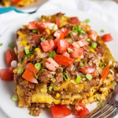Mexican lasagna recipe served on a white plate with tomatoes and green onions