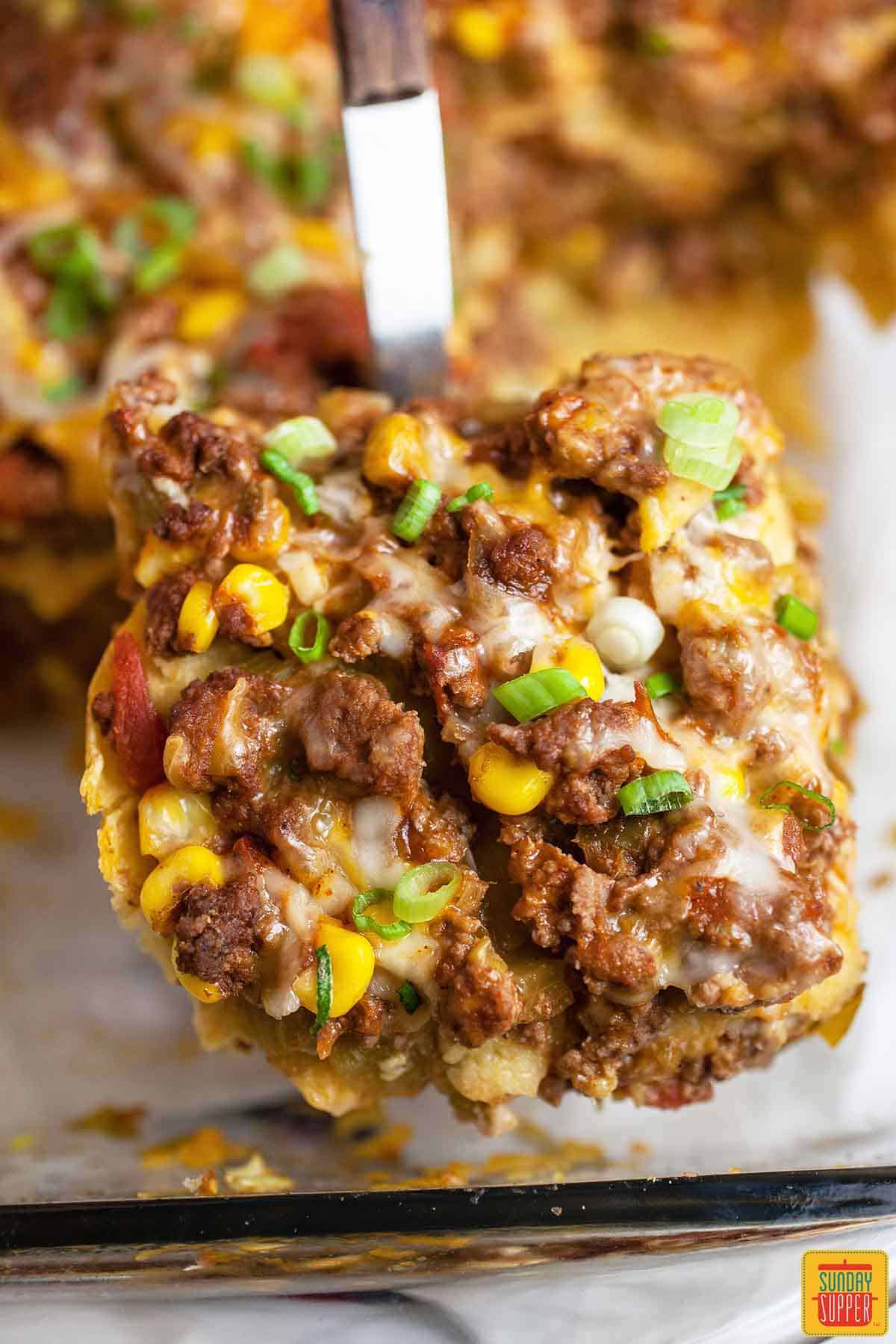 Lifting Mexican lasagna with corn tortillas out of a casserole dish with a spatula