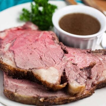 Boneless prime rib roast slices on a white plate with a cup of au jus