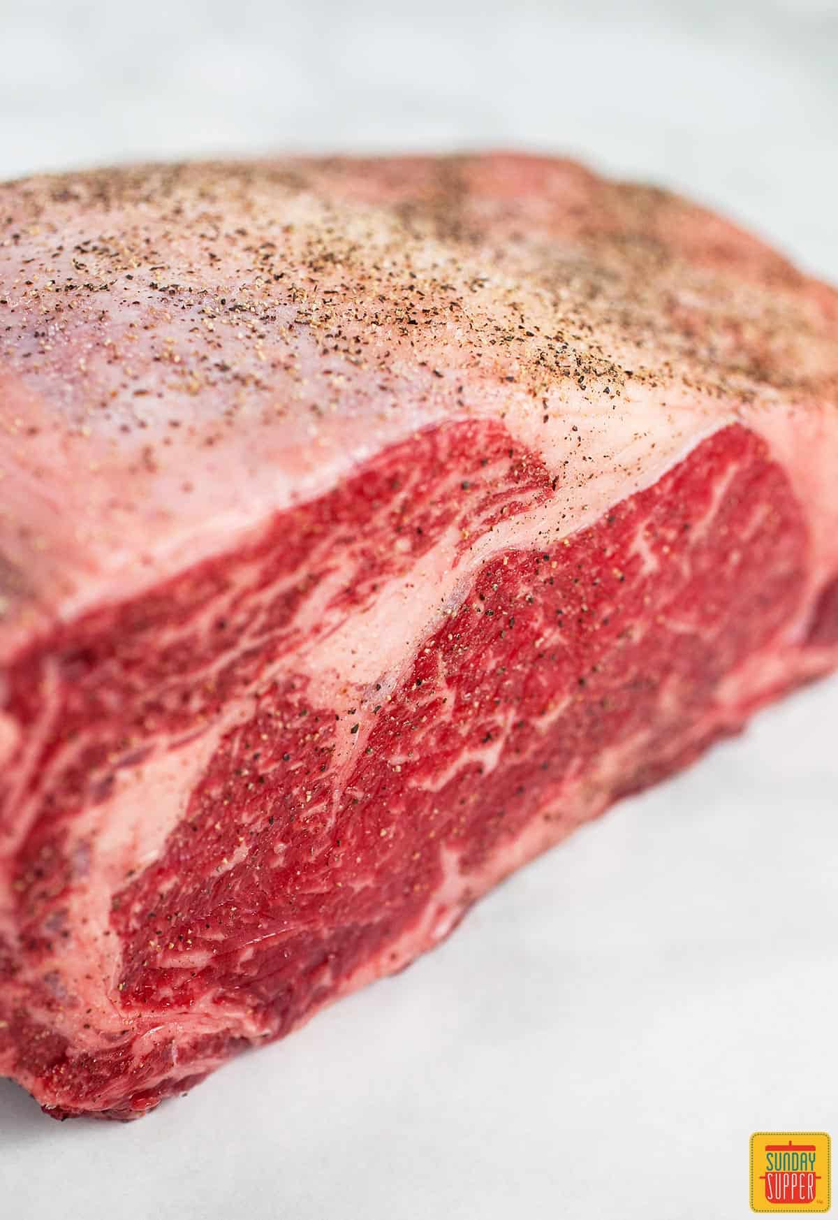 A raw rib roast coated with salt and pepper on a white surface