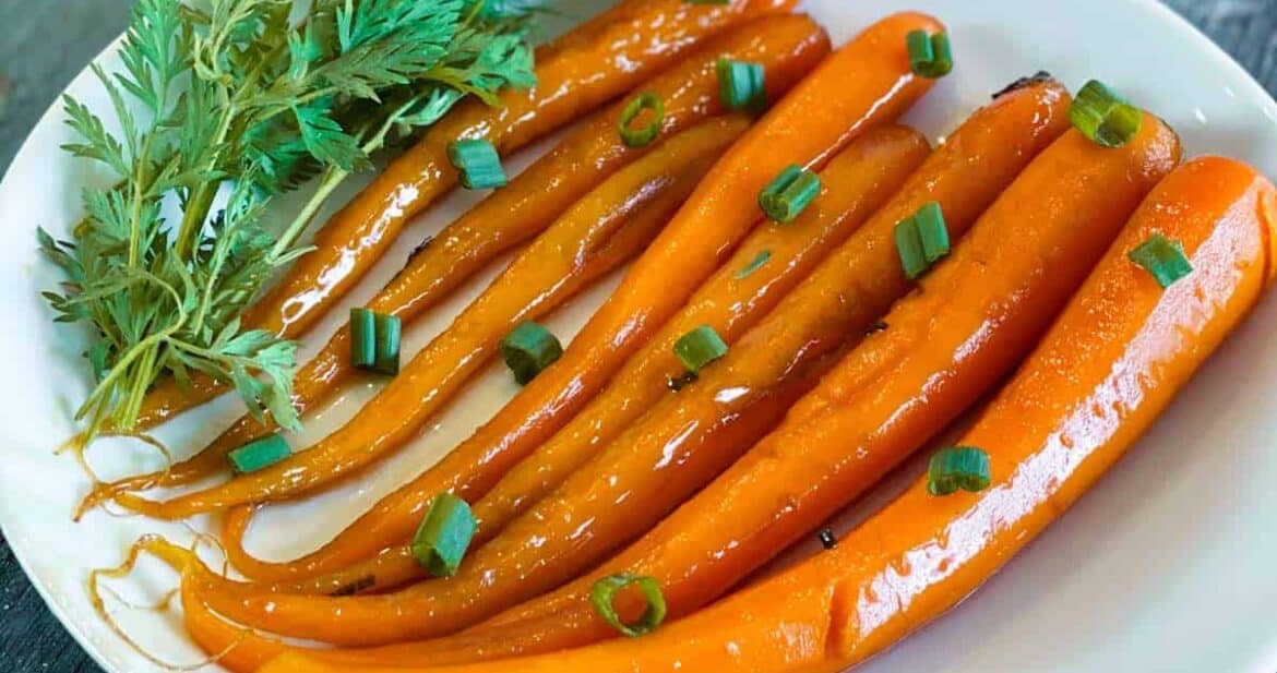 Candied carrots on a white plate with fresh herbs and green onions